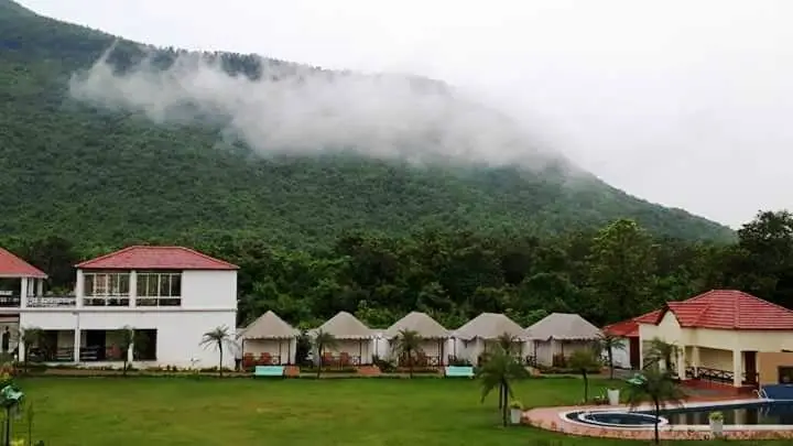 Resort cottages with red roofs at Garh Panchkot, Purulia, surrounded by green hills and misty clouds.